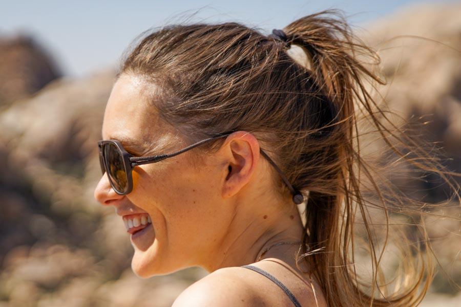 MATTEBROWN_BROWN Side shot of woman in rocks smiling wearing Ombraz classic armless strap sunglasses