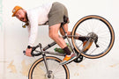 MATTEBROWN_GREY Man doing a wheelie on a bike hanging a pair or Ombraz classic armless sunglasses with strap around his neck