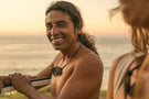 leggero_charcoal_grey Man at the beach smiling wearing Ombraz leggero armless strap sunglasses around his neck