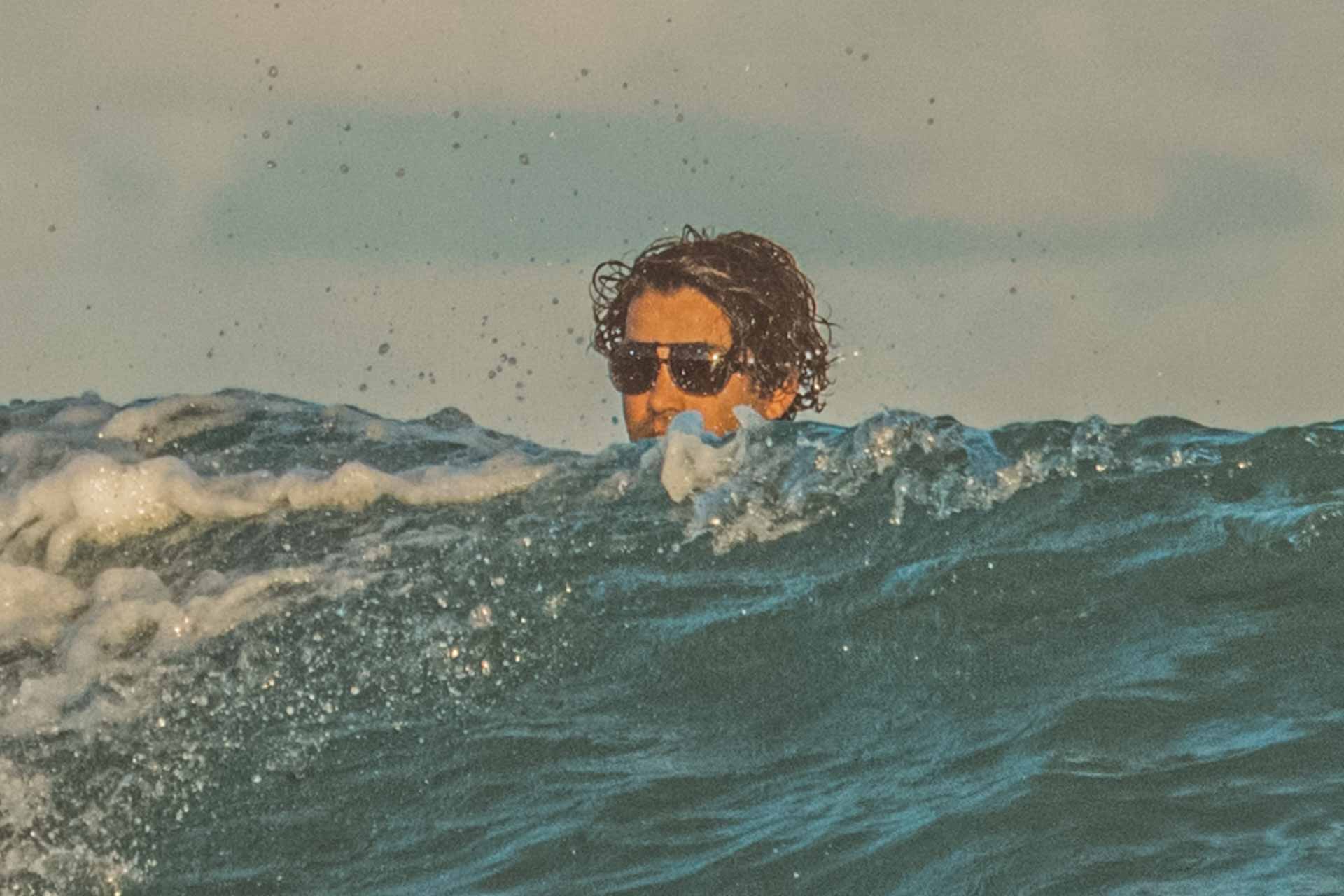 leggero_charcoal_grey Man's head poking out from above a wave wearing Ombraz leggero armless sunglasses