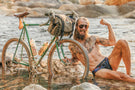 mattebrown_brown Man at the beach resting next to his bike wearing Ombraz classic matte brown sunglasses with cord