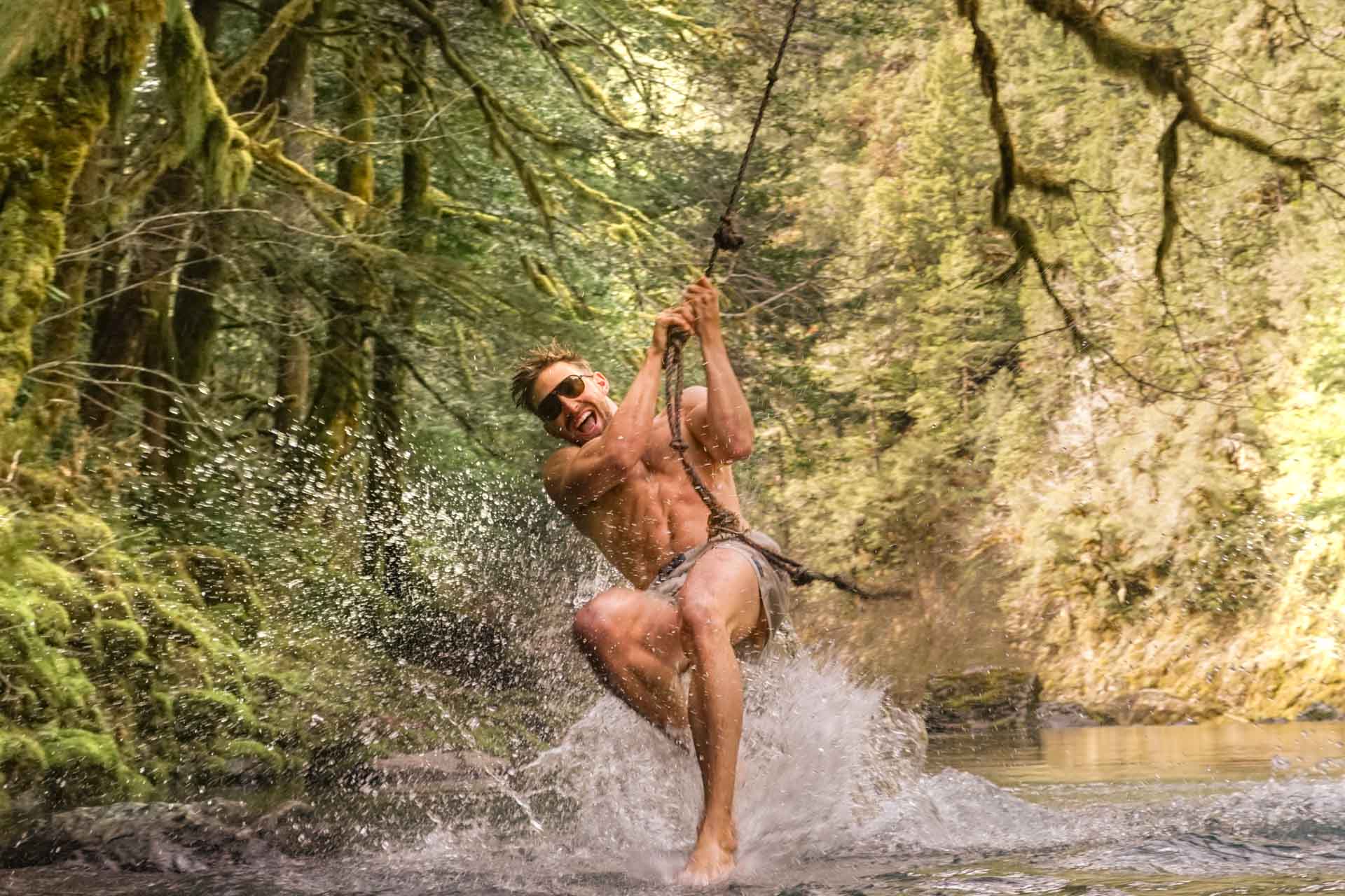 mattebrown_brown Man on a rope swing in a river smiling wearing Ombraz classic armless string sunglasses