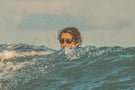 leggero_tortoise_brown Man riding a wave wearing Ombraz leggero armless sunglasses with cord