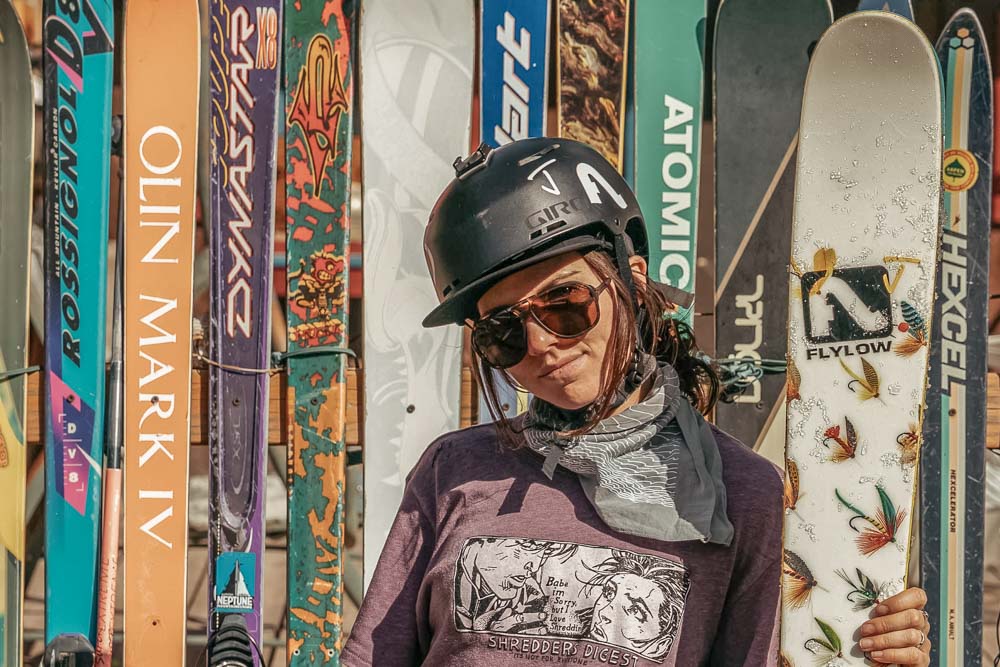 Tortoise_brown Female skier wearing ombraz classic armless rope sunglasses in front of a collection of skis