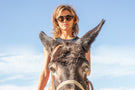 Woman riding a donkey wearing Ombraz armless viale sunglasses VIALE_CHARCOAL_BROWN