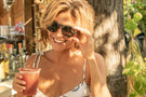 VIALE_DUSK_BROWN Woman holding a drink smiling wearing Ombraz viale armless sunglasses with cord